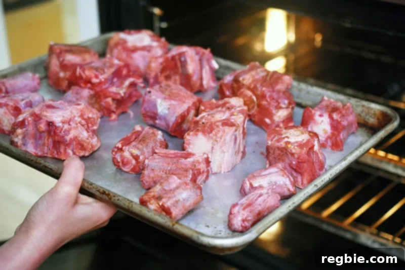 A baking sheet with seasoned oxtails is placed in the oven.