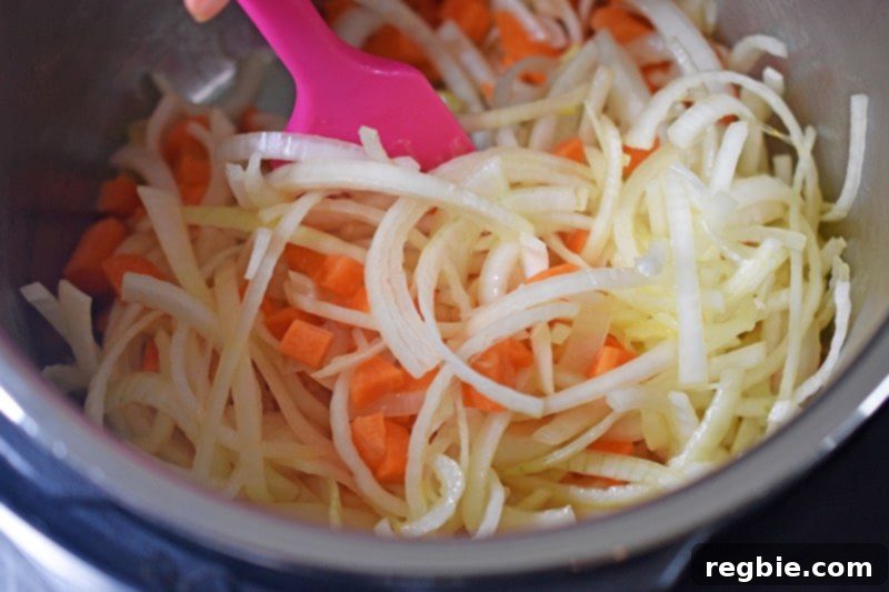 A closeup of diced carrots and sliced onions being sautéed in an open Instant Pot.