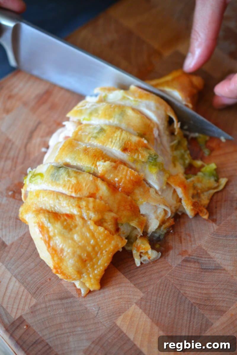 An overhead shot of Ginger-Scallion Chicken being sliced on a wooden cutting board, showcasing golden skin and tender meat.
