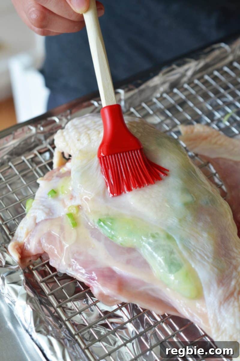 Melted fat being brushed on top of the Ginger-Scallion Chicken with a red silicone brush, preparing it for roasting.