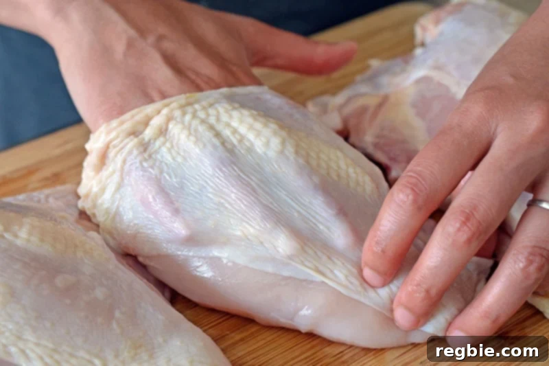 A hand gently loosening the skin between the chicken skin and the breast to form a pocket for the sauce.