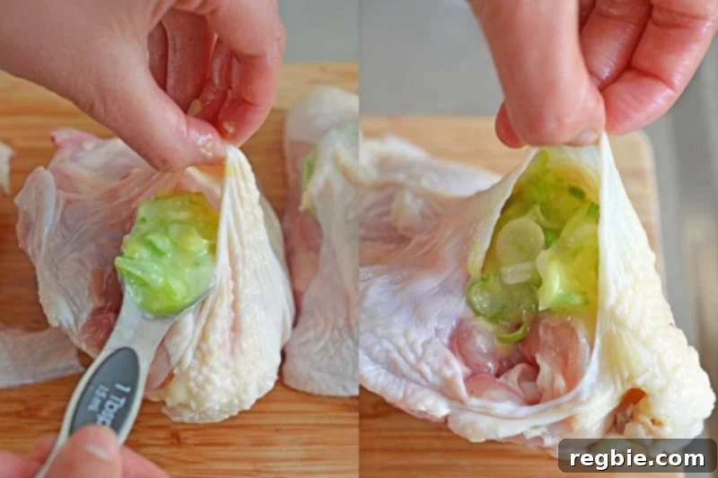 Spoonful of ginger-scallion sauce being placed under the skin of a piece of chicken breast.