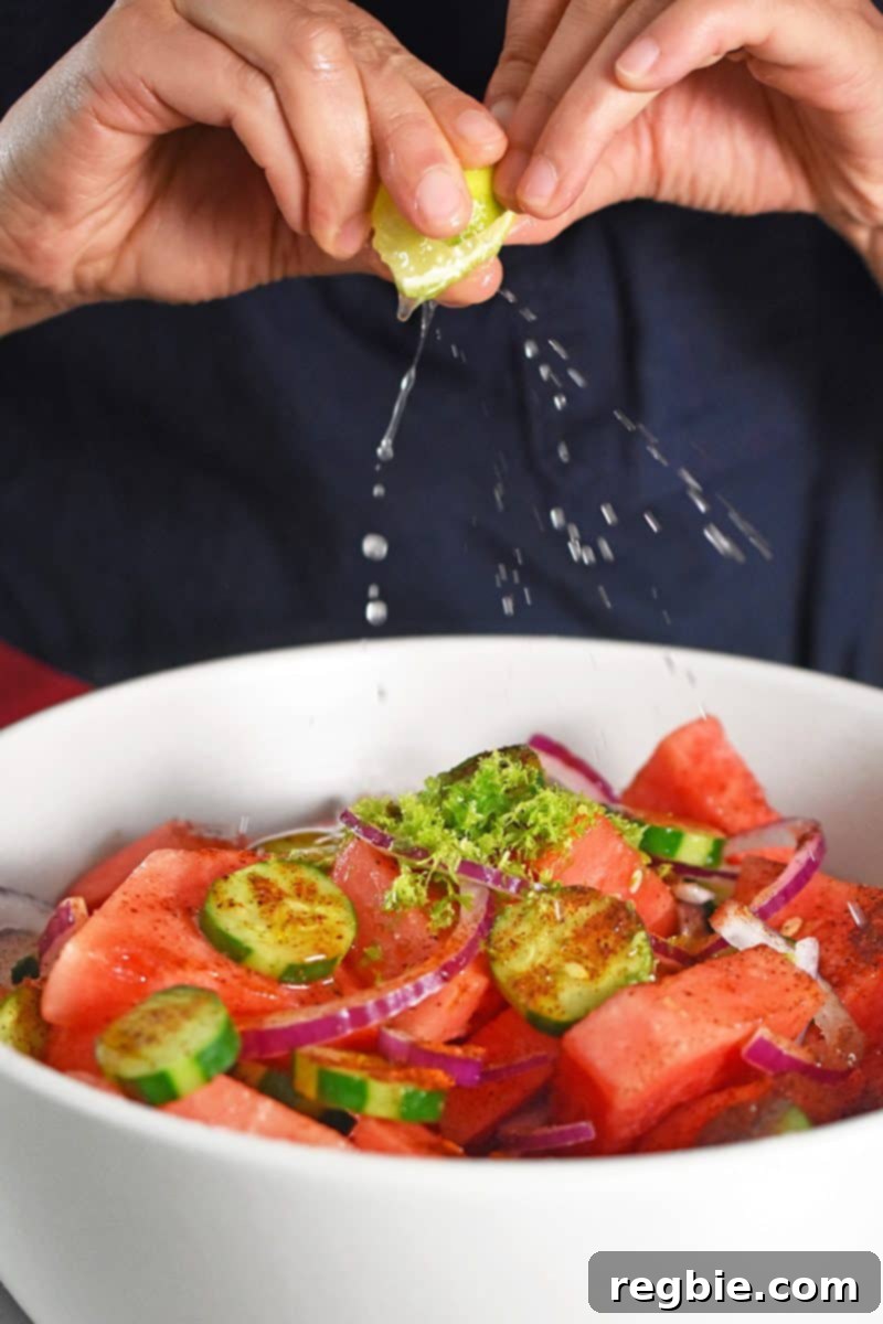 Fiesta Watermelon Cucumber Salad 9 Someone squeezing fresh lime juice over the paleo Mexican watermelon salad ingredients in a bowl.