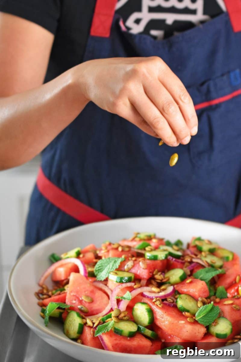 Fiesta Watermelon Cucumber Salad 10 Someone garnishing the vibrant Mexican watermelon and cucumber salad with fresh mint leaves and crunchy pepitas.