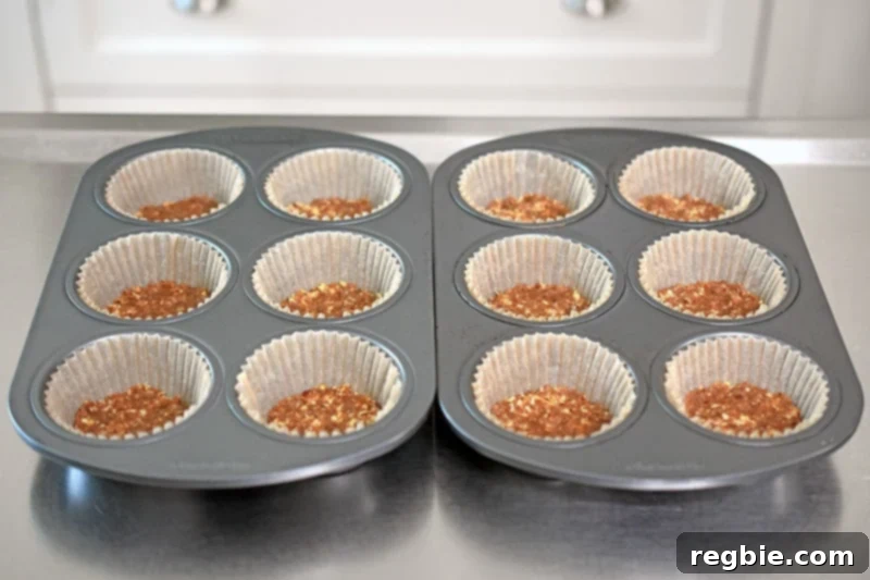 A shot of muffin tins filled with parchment cups, each containing a flattened No-Bake Matcha Cheesecake crust base.