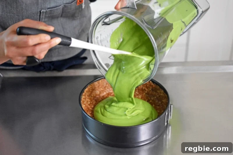 Transferring the bright-green No-Bake Matcha Cheesecake filling into the springform pan over the prepared crust.