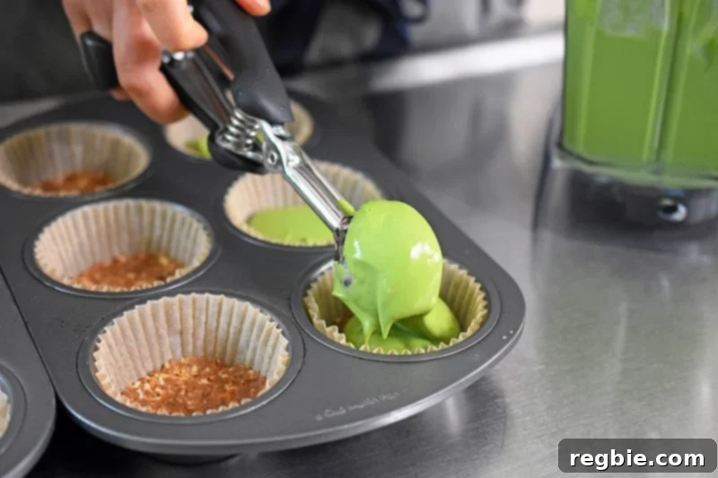 Scooping the No-Bake Matcha Cheesecake filling into individual cupcake holders for mini cheesecakes.