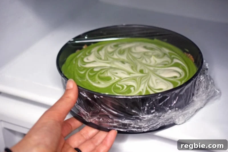 A paleo No-Bake Matcha Cheesecake covered with plastic wrap, placed in the refrigerator (or freezer) to chill and set.