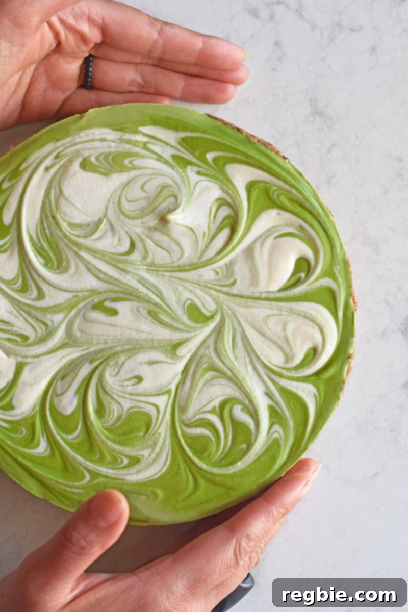 An overhead shot of a vibrant, healthy paleo No-Bake Matcha Cheesecake with a bright green and white swirled top, ready to be served.