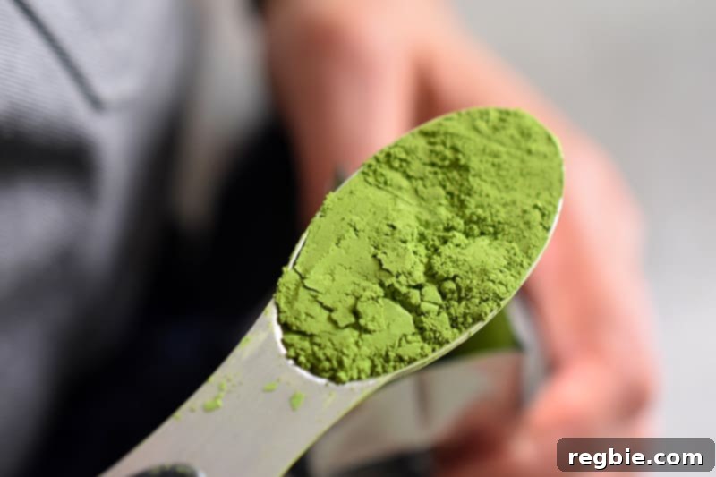 An overhead shot of a spoonful of bright green ceremonial grade matcha powder, essential for a vibrant No-Bake Matcha Cheesecake.