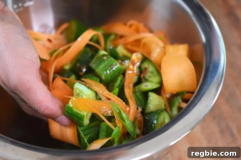 Someone tossing the ingredients for paleo and whole30 smashed cucumber and carrot salad in a bowl.
