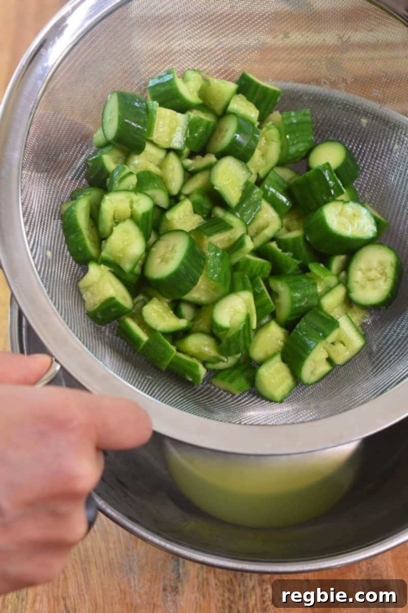 Taking the cucumbers in the colander or fine mesh strainer out of the metal bowl.