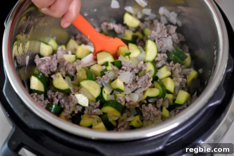 An overhead shot of someone stirring the Instant Pot Zucchini Bolognese ingredients vigorously in an open Instant Pot, ensuring everything is well combined.