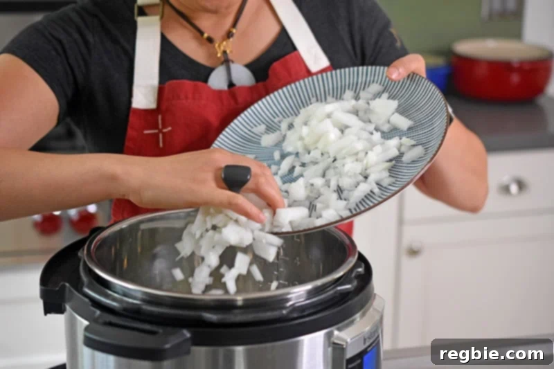 Someone carefully adding diced onions to an open Instant Pot, beginning the sautéing process.