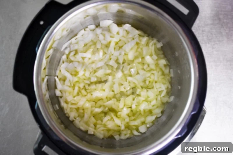 An overhead shot showcasing diced onions gently sautéing in olive oil within an open Instant Pot, turning translucent.