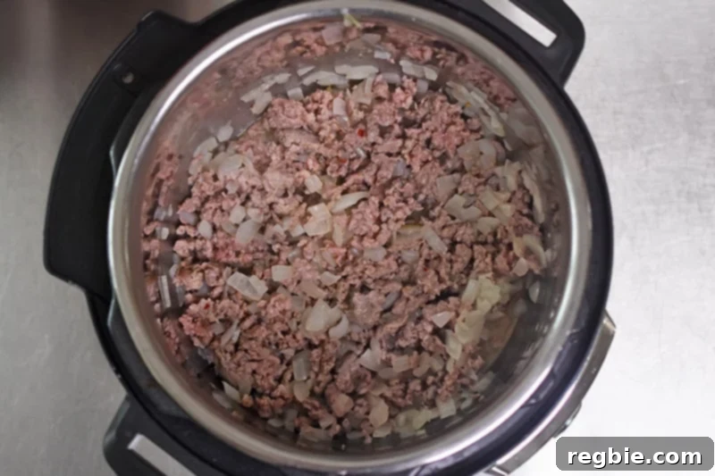 An overhead shot of perfectly cooked Italian sausage mixed with softened onions in an open Instant Pot, ready for the next steps.
