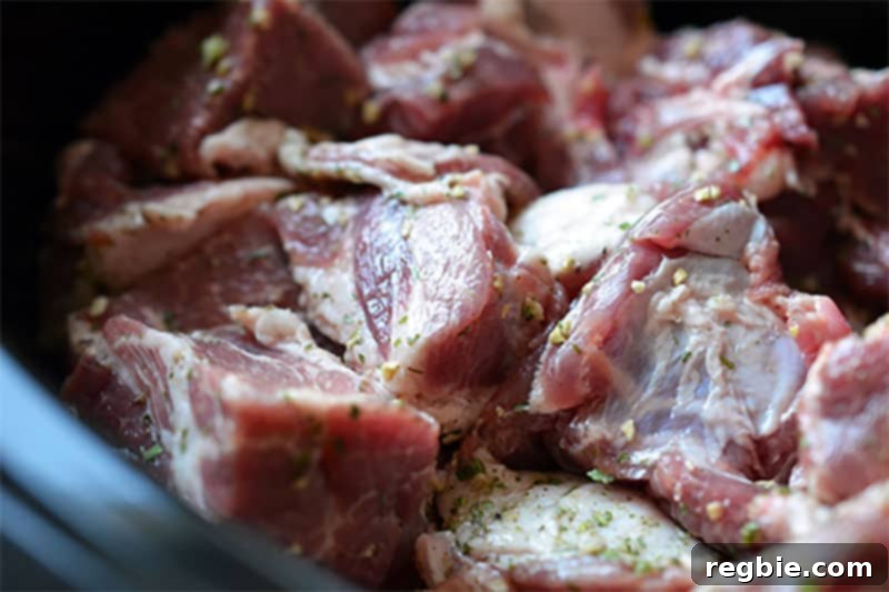 Seasoned pork shoulder cubes layered over a bed of onions and carrots in the slow cooker, forming the hearty base for the stew.