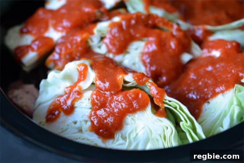Rich red marinara sauce being drizzled over the cabbage wedges and other ingredients in the slow cooker, completing the layering for the Cheater Pork Stew.