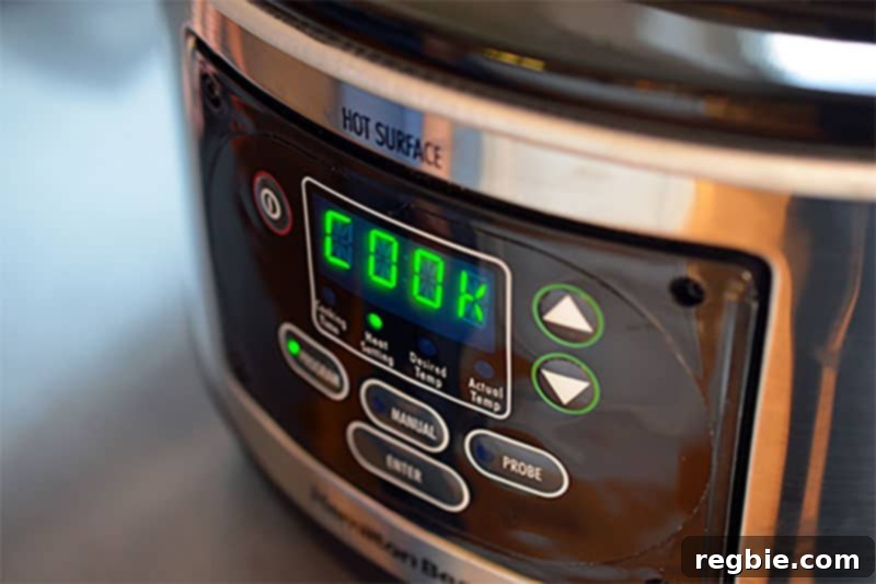 A close-up of a slow cooker's digital display, showing the 'Low' setting, indicating it's gently cooking a batch of Slow Cooker Cheater Pork Stew, a simple and healthy Paleo and Whole30 meal.