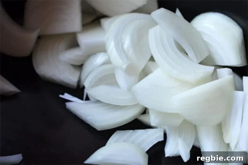 Thinly sliced white onions and smashed garlic cloves on a dark cutting board, ready to be added to the Slow Cooker Cheater Pork Stew.