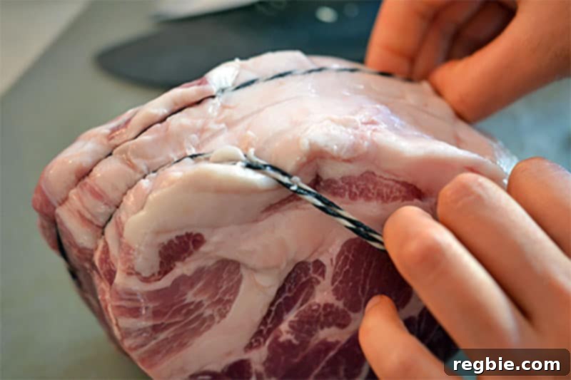Hands carefully removing butcher twine from a pork shoulder roast, preparing it for cubing and slow cooking in the Cheater Pork Stew recipe.