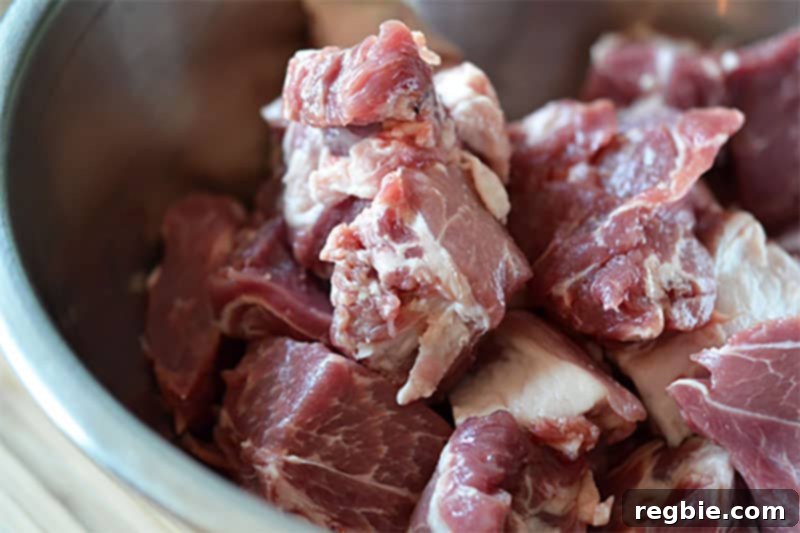 A metal bowl filled with evenly cubed pork shoulder, cut into 1.5-inch pieces, ready to be seasoned for the Slow Cooker Cheater Pork Stew.