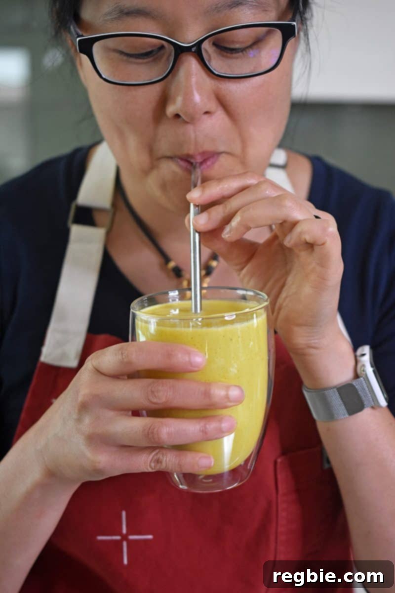 Sun-Kissed Wellness Smoothie 2 Michelle Tam sipping a vibrant paleo golden glow smoothie through an elegant metal straw, conveying refreshment and health.