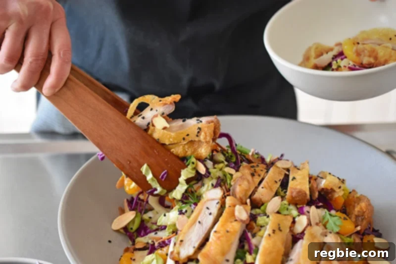 A pair of wooden tongs are used to transfer the vibrant, Whole30-friendly Chinese Chicken Salad into a serving bowl. This gluten-free Chinese Chicken Salad is truly the best!