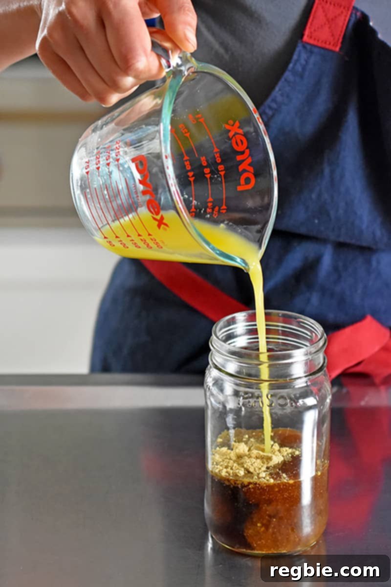 A close-up shot of orange juice being poured into a mason jar already containing other ingredients for the All-Purpose Stir-Fry Sauce, demonstrating the ease of preparation.