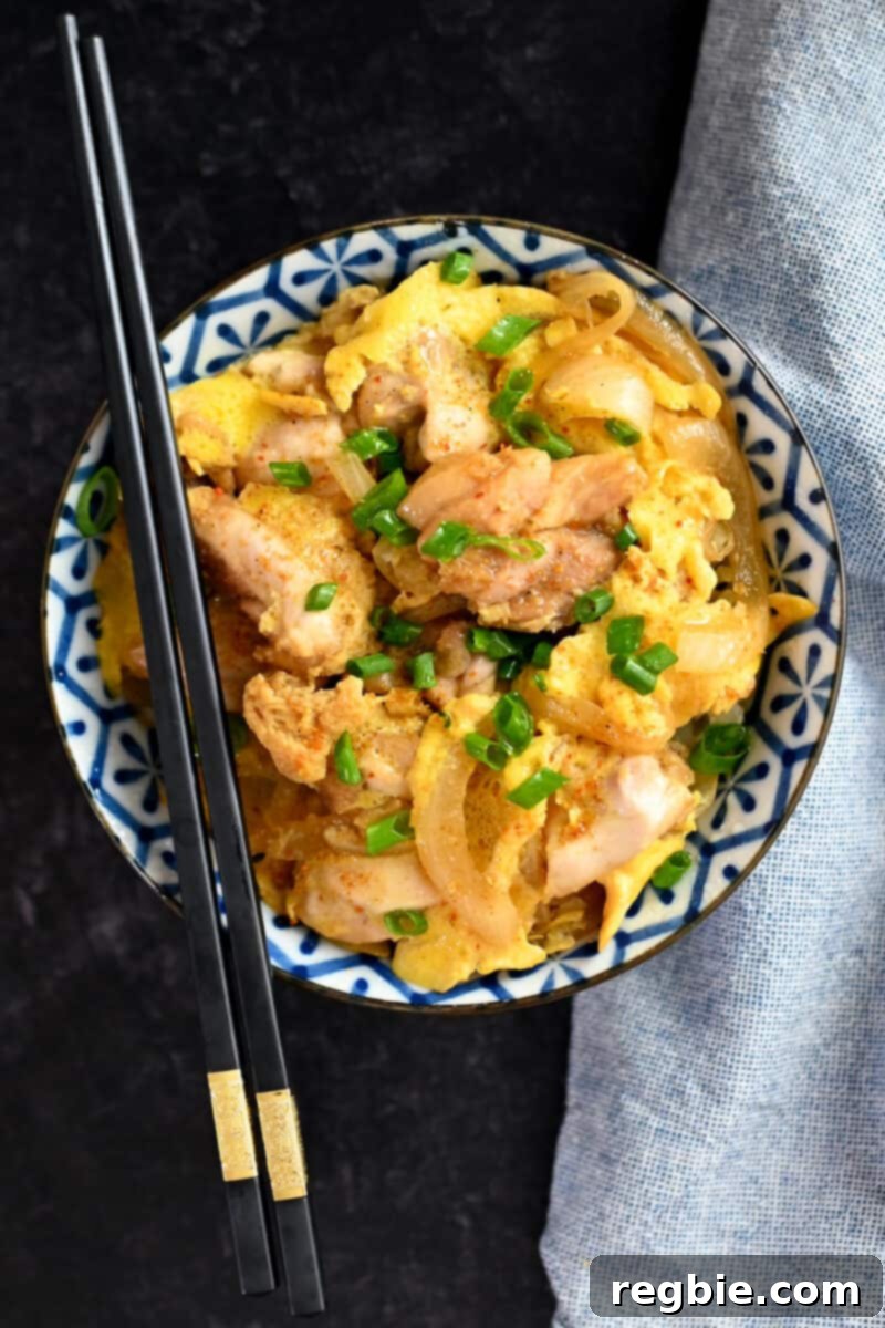 An inviting overhead shot of a bowl brimming with paleo and low-carb Oyakodon, a Japanese chicken and egg bowl, with a pair of black chopsticks resting gracefully on the rim.