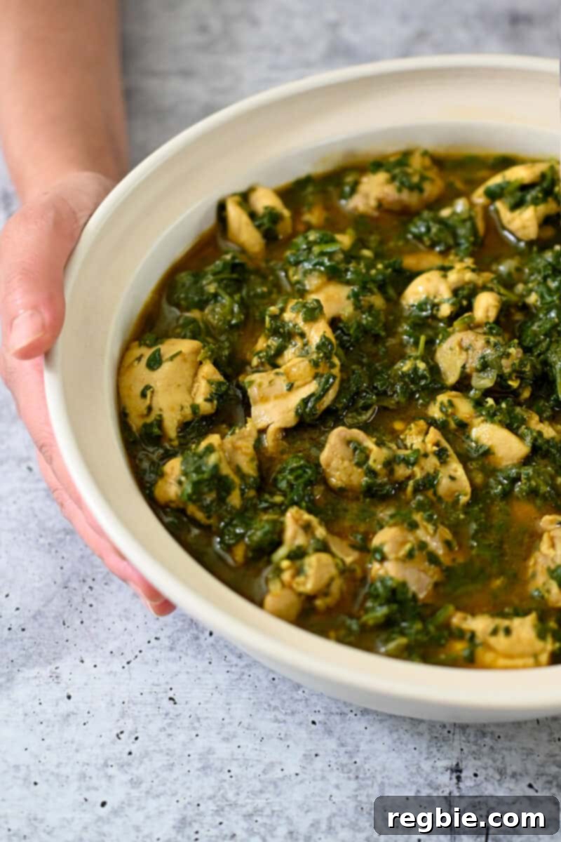 Primal Instant Pot Perfection 7 A hand is holding an elegant, off-white bowl filled with flavorful chicken and spinach Indian curry, freshly prepared.
