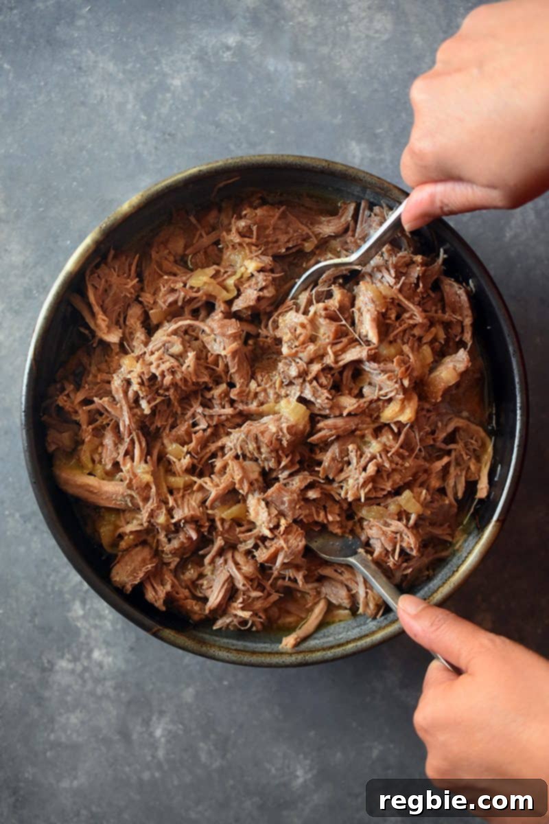 An overhead shot of Instant Pot Magic Pork in a large bowl being served with two forks, showcasing its tender, shredded texture.