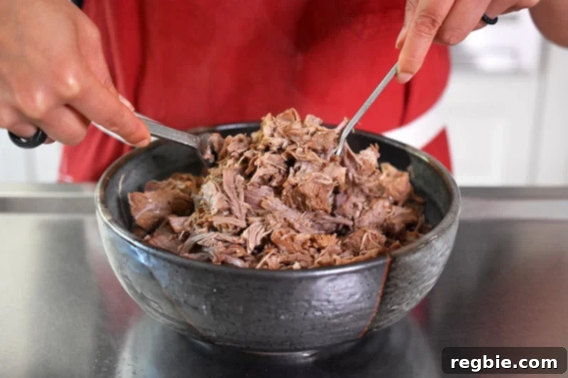 Shredding the perfectly cooked Instant Pot Magic Pork in a large bowl using two forks, revealing its juicy, tender texture.