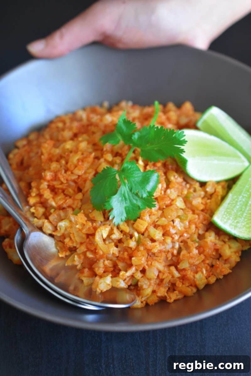 A bowl of Whole30 and Paleo Mexican cauliflower fried rice, generously topped with fresh cilantro and vibrant lime wedges, ready to be enjoyed.