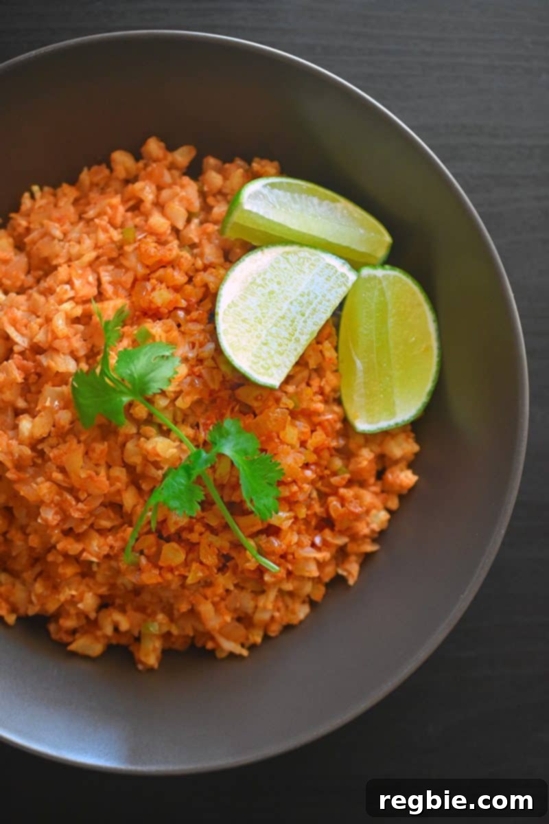 An overhead shot showcasing Mexican Cauliflower Rice in a bowl, garnished with fresh cilantro and bright lime wedges, ready to be enjoyed.