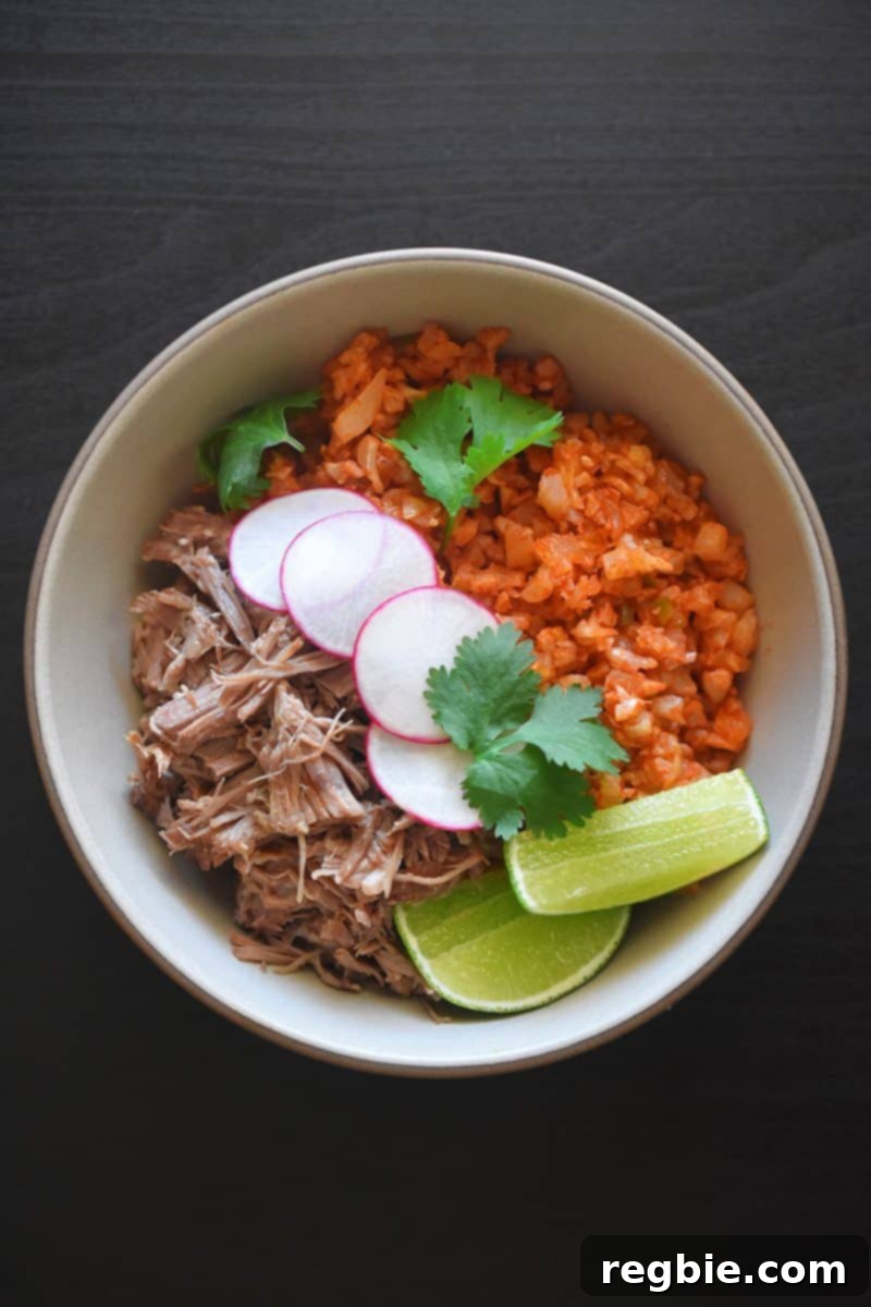 An inviting overhead view of a colorful Whole30 burrito bowl featuring Mexican Cauliflower Rice, tender carnitas, fresh lime slices, and crisp radishes.
