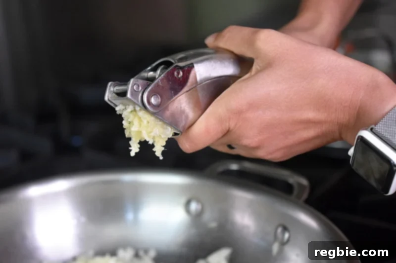 Minced garlic is being added to the sautéed onions in the pan, infusing the low-carb Mexican Cauliflower rice with aromatic flavor.