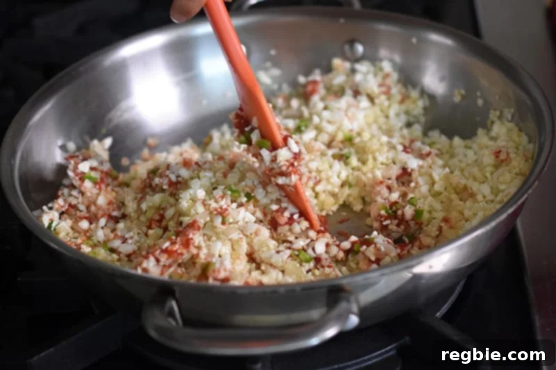 The paleo Mexican cauliflower rice is being expertly stirred in a skillet with a silicone spatula, ensuring all ingredients are fully blended.