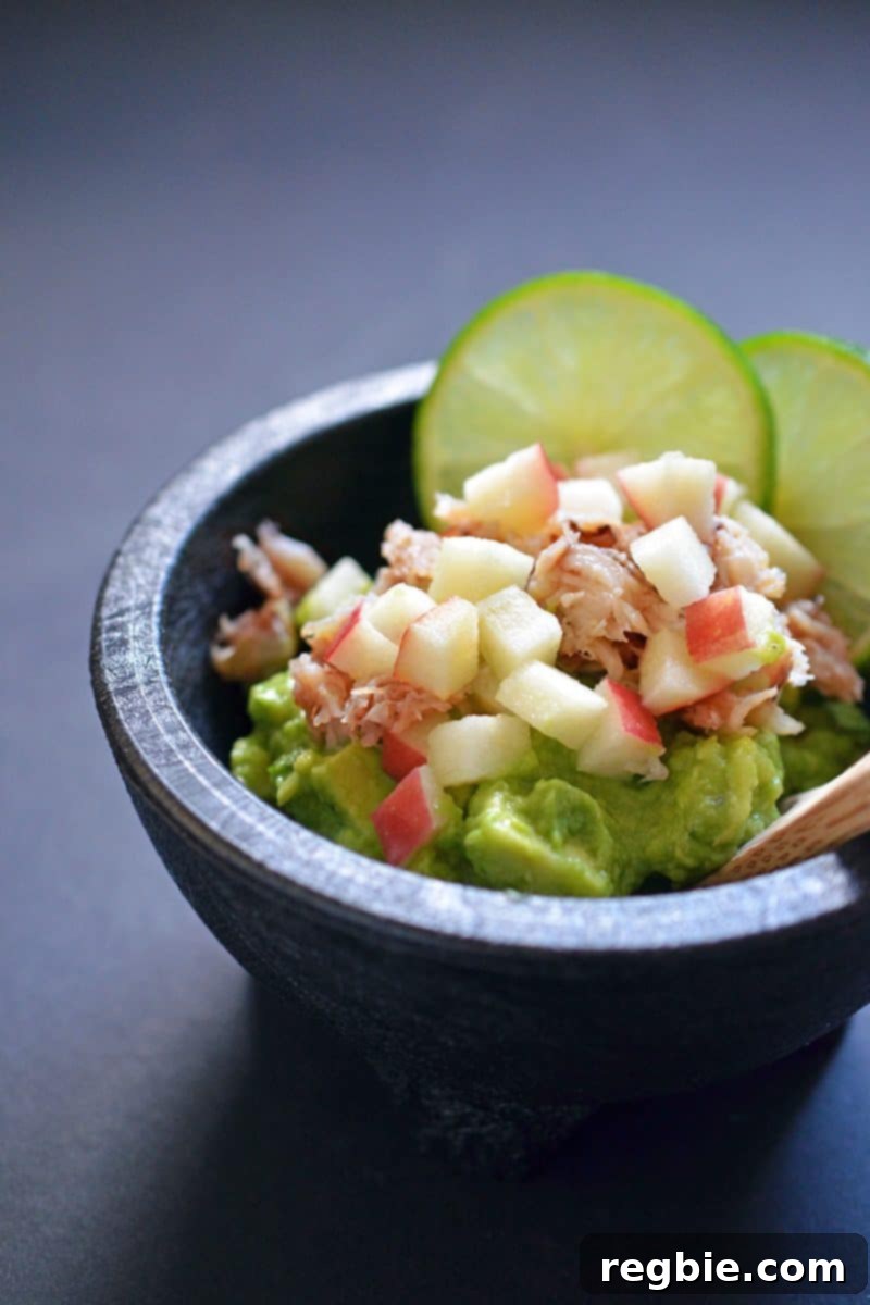 Avocado Dream Dip 11 Guacamole served in a traditional black molcajete, generously topped with delicate lump crab meat, finely diced crisp apples, and fresh lime slices, creating an elegant and flavorful appetizer.