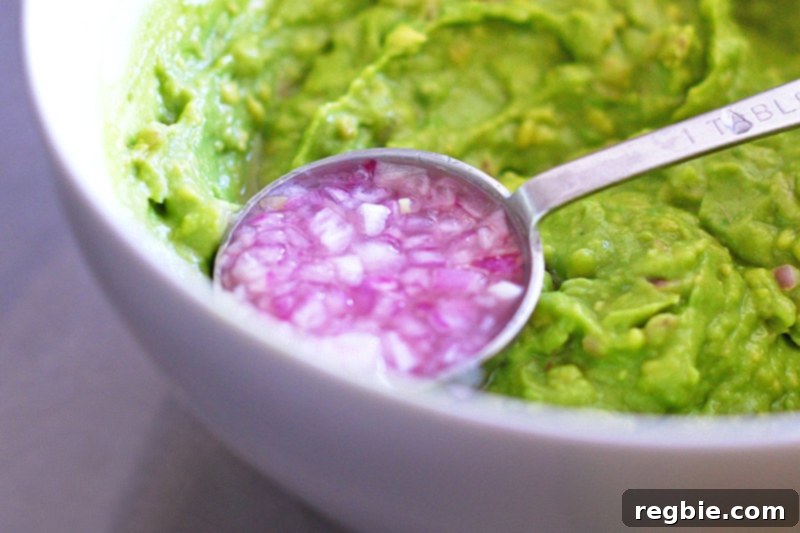 Avocado Dream Dip 6 A tablespoon filled with the bright lime-shallot-salt mixture being carefully added to the creamy mashed avocado.