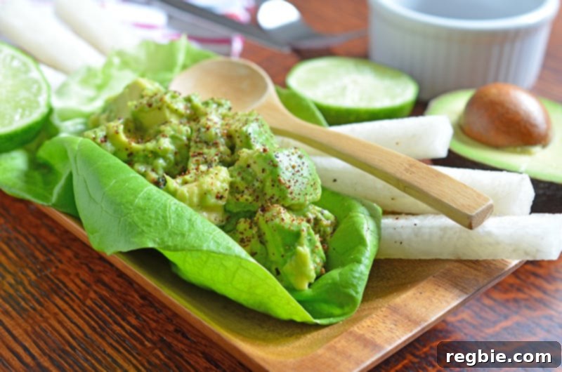Avocado Dream Dip 10 A healthy lettuce taco filled with creamy guacamole, accompanied by fresh jicama sticks, vibrant lime halves, and elegant serving spoons, highlighting a fresh meal.