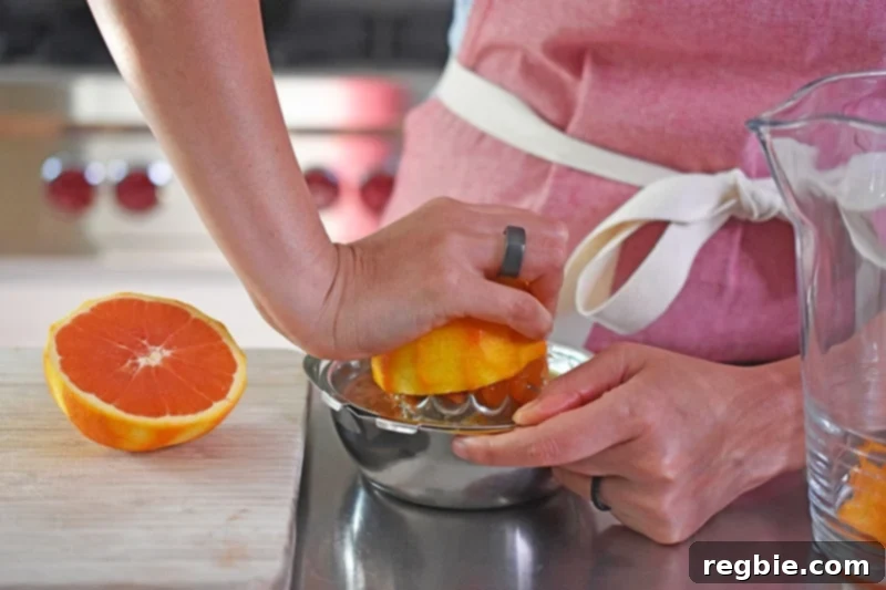 A person in a red apron is juicing a half of an orange with a manual juicer.