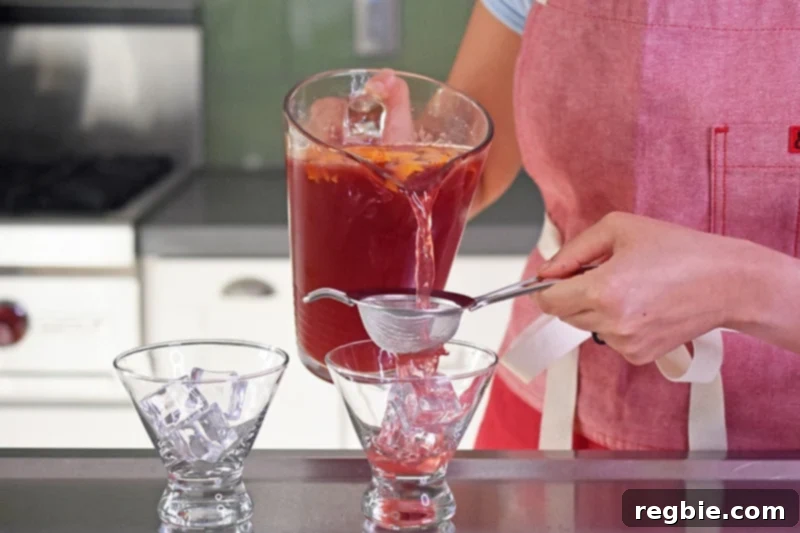 Pouring a pomegranate orange juice mocktail through a strainer and into a fancy glass for serving.