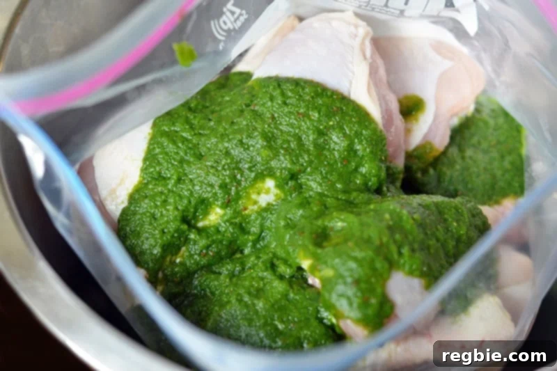 An overhead view of raw chicken in a Ziplock bag, now fully coated with the bright green Paleo marinade.