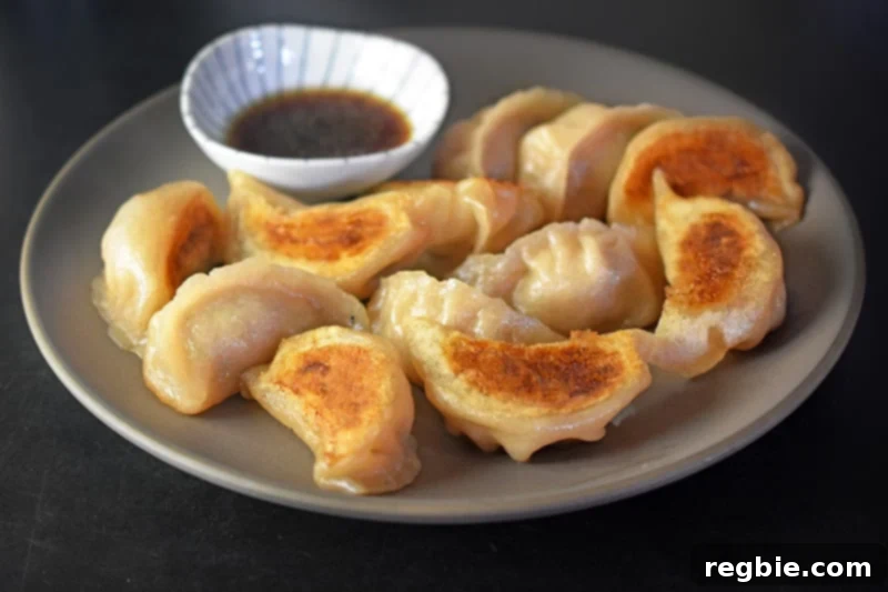 A close up of Paleo Pot Stickers with crispy golden bottoms and a dish of dipping sauce in the background.