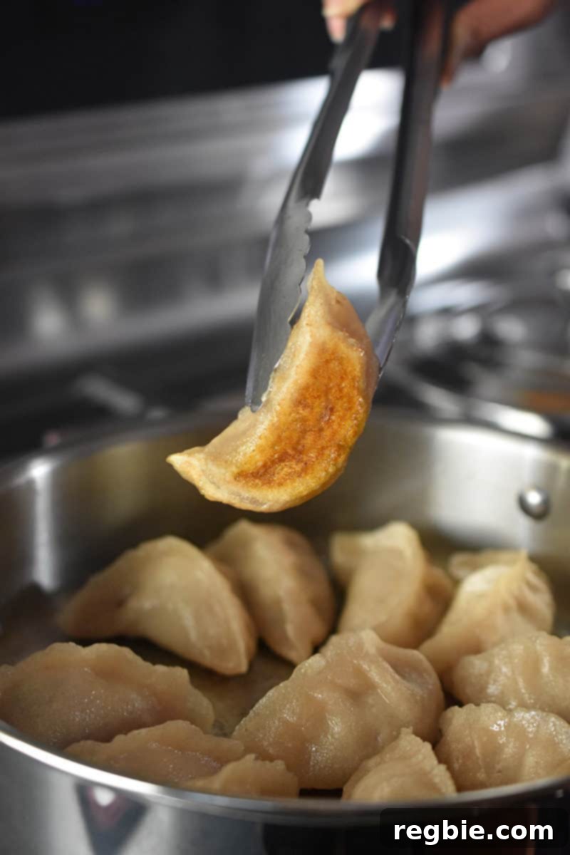 A pair of tongs is lifting up a cooked pot sticker, showing the crispy golden bottom.