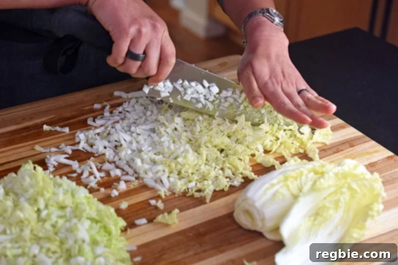 A small napa cabbage is finely chopped on a large wooden cutting board.
