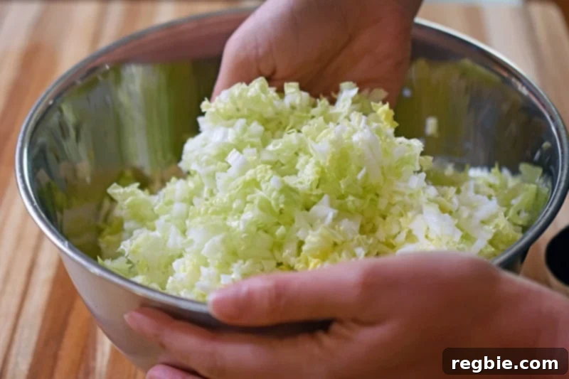 The finely minced napa cabbage and kosher salt are tossed by hand in a large metal bowl.
