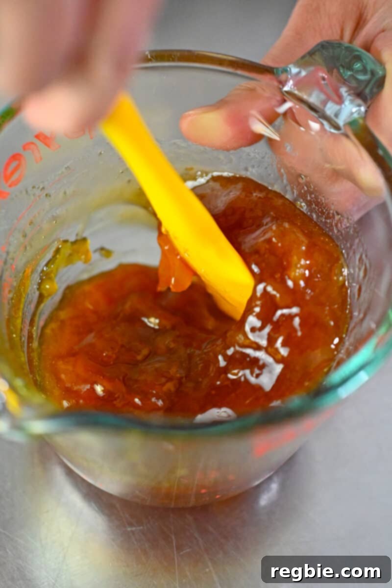 Effortless Peach Glazed Pork Roast 11 An overhead shot of a measuring cup filled with a peach jam glaze that is being stirred with a yellow silicone spatula.