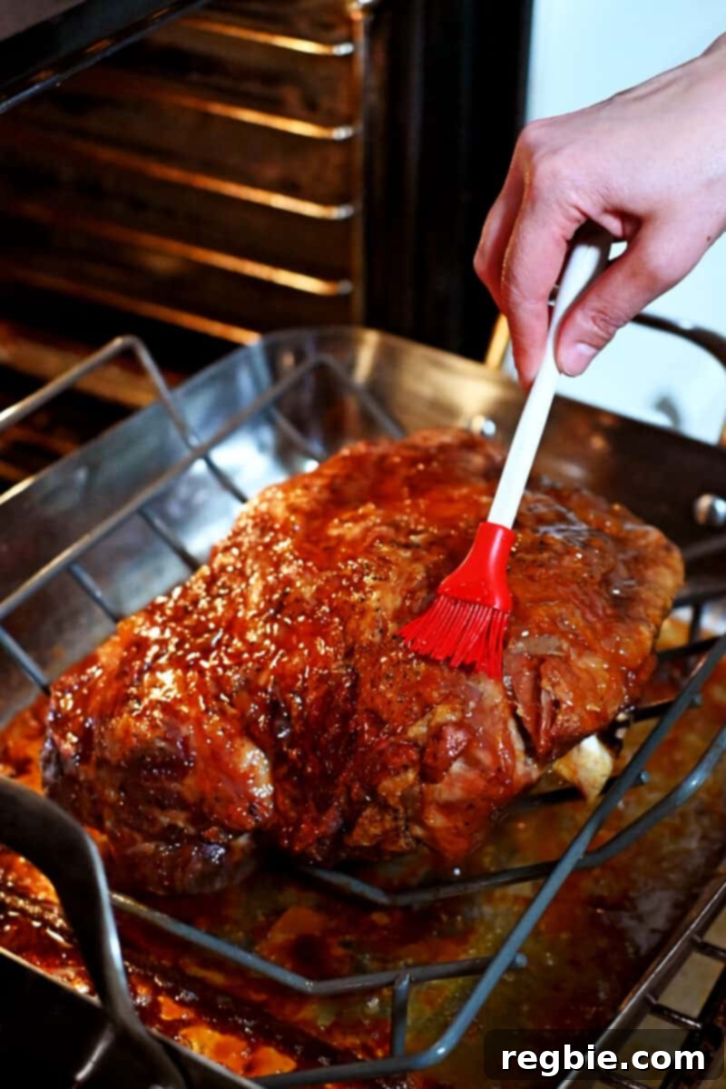 Effortless Peach Glazed Pork Roast 12 A silicone brush is adding a peach jam glaze onto a golden brown pork shoulder roast in the oven.